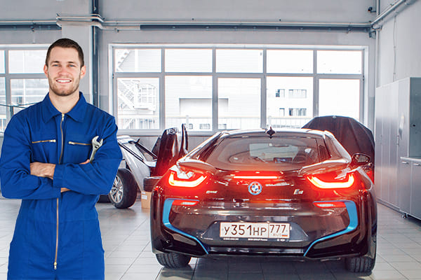 A repair mechanic with the rear of a black BMW sports car behind him